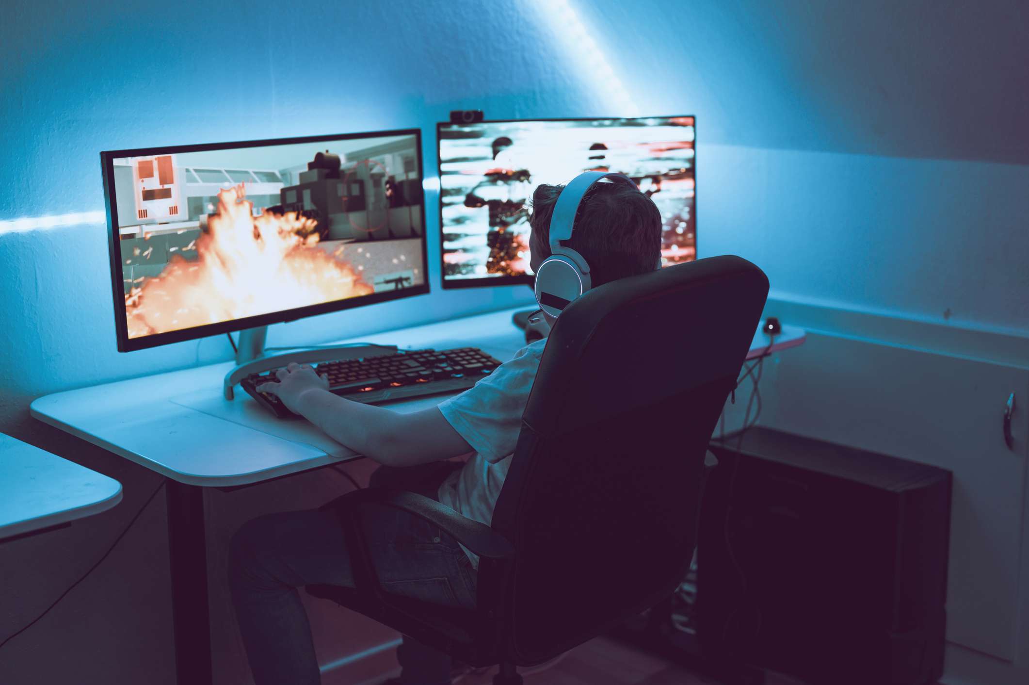 A boy plays video game online and sits in front of two big computer monitors.