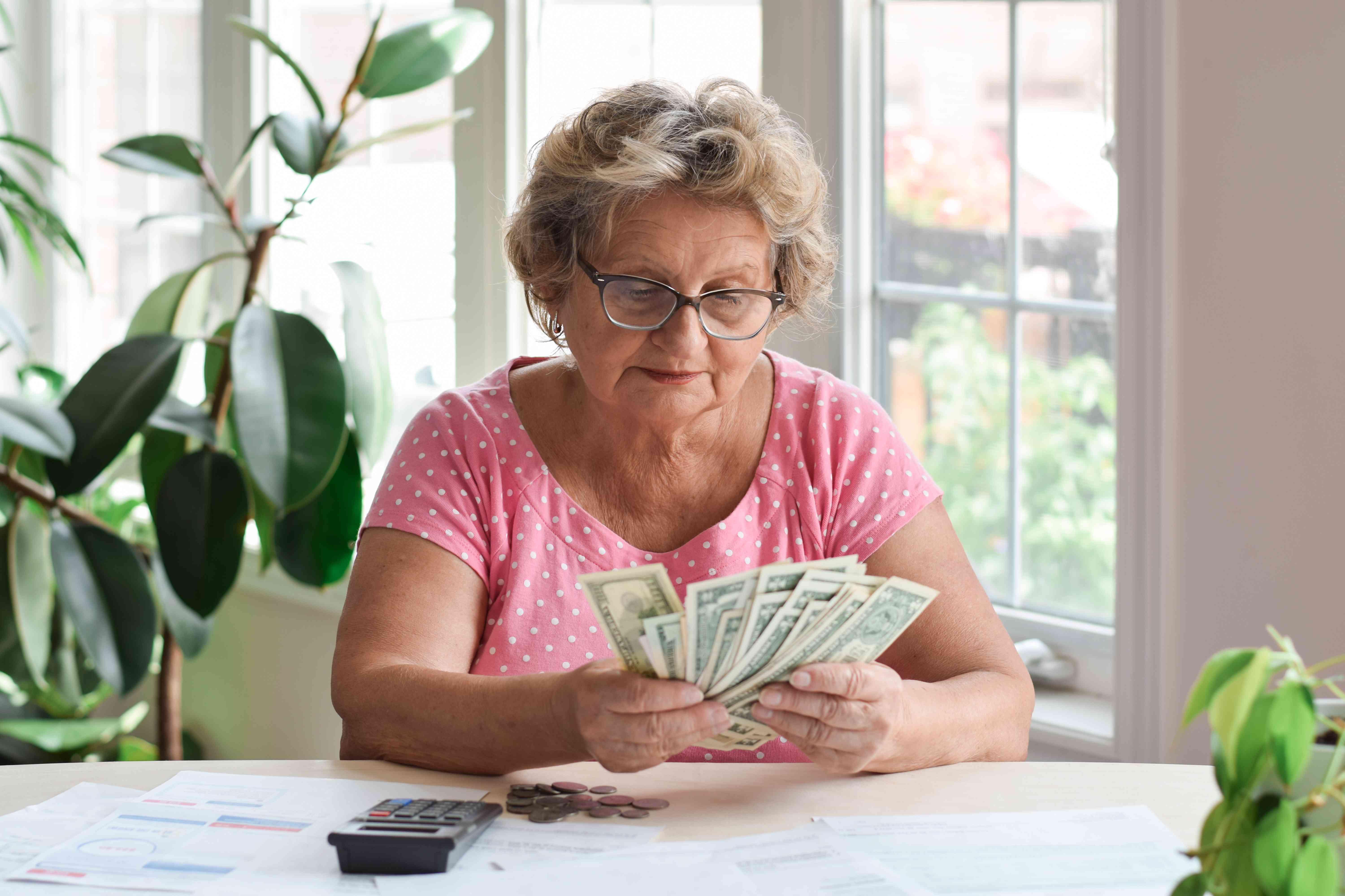 Senior woman sitting at home counting paper money and some pennies