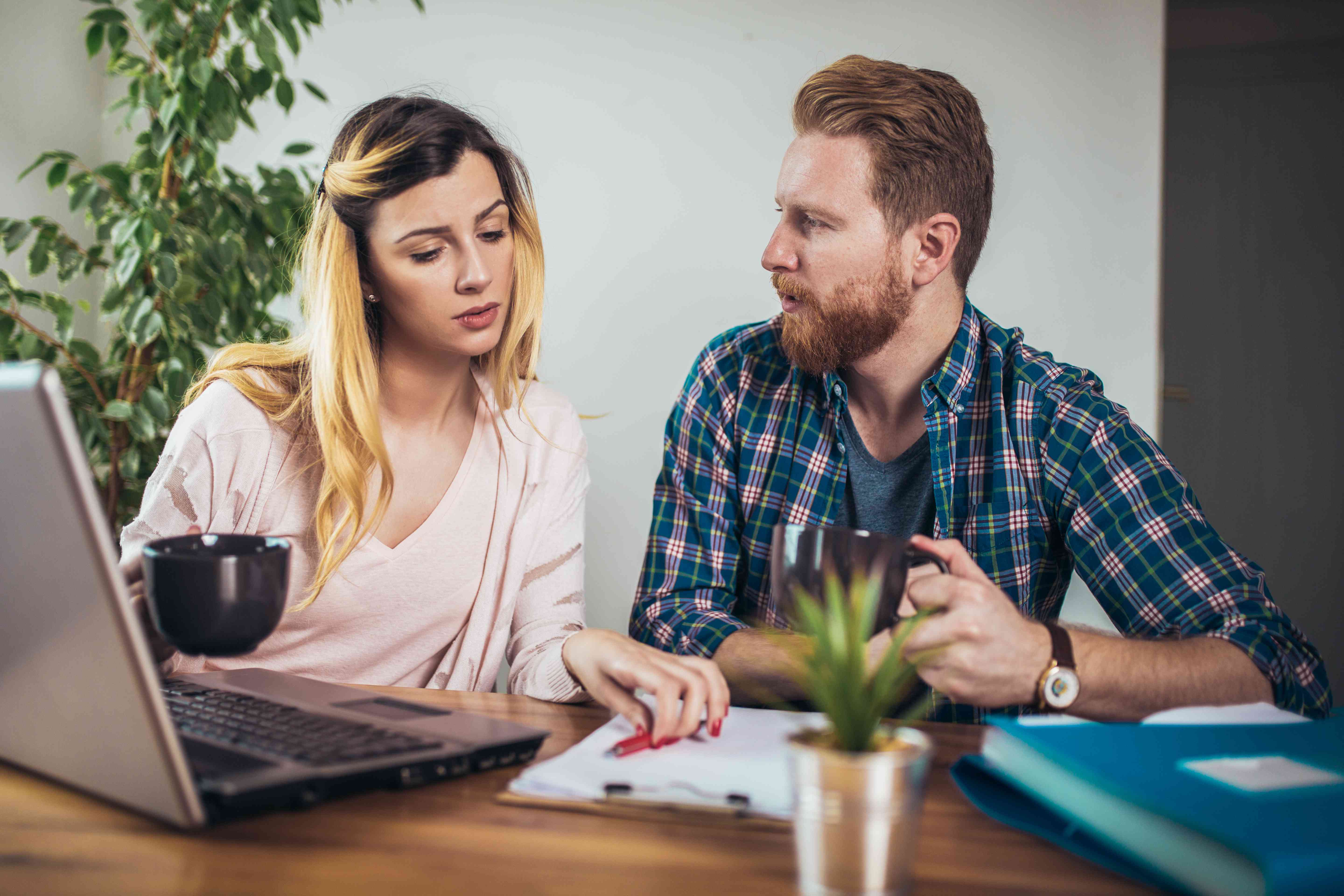 Young couple sitting together at their dining room table and looking at a laptop and documents