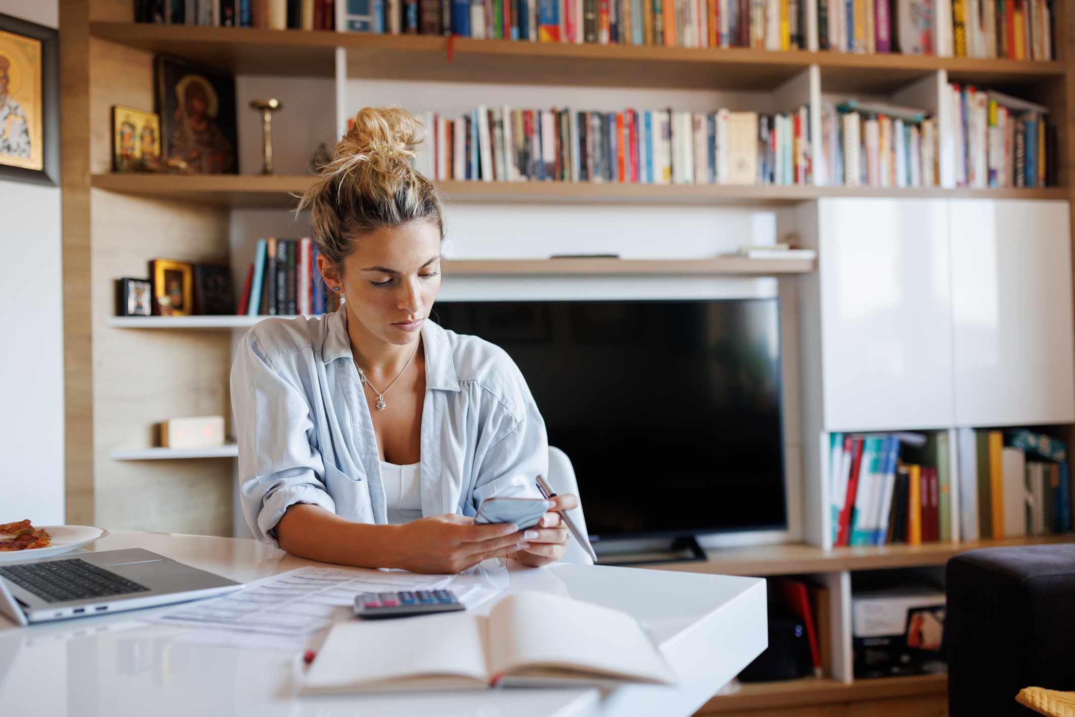 A woman uses a phone at a home desk.