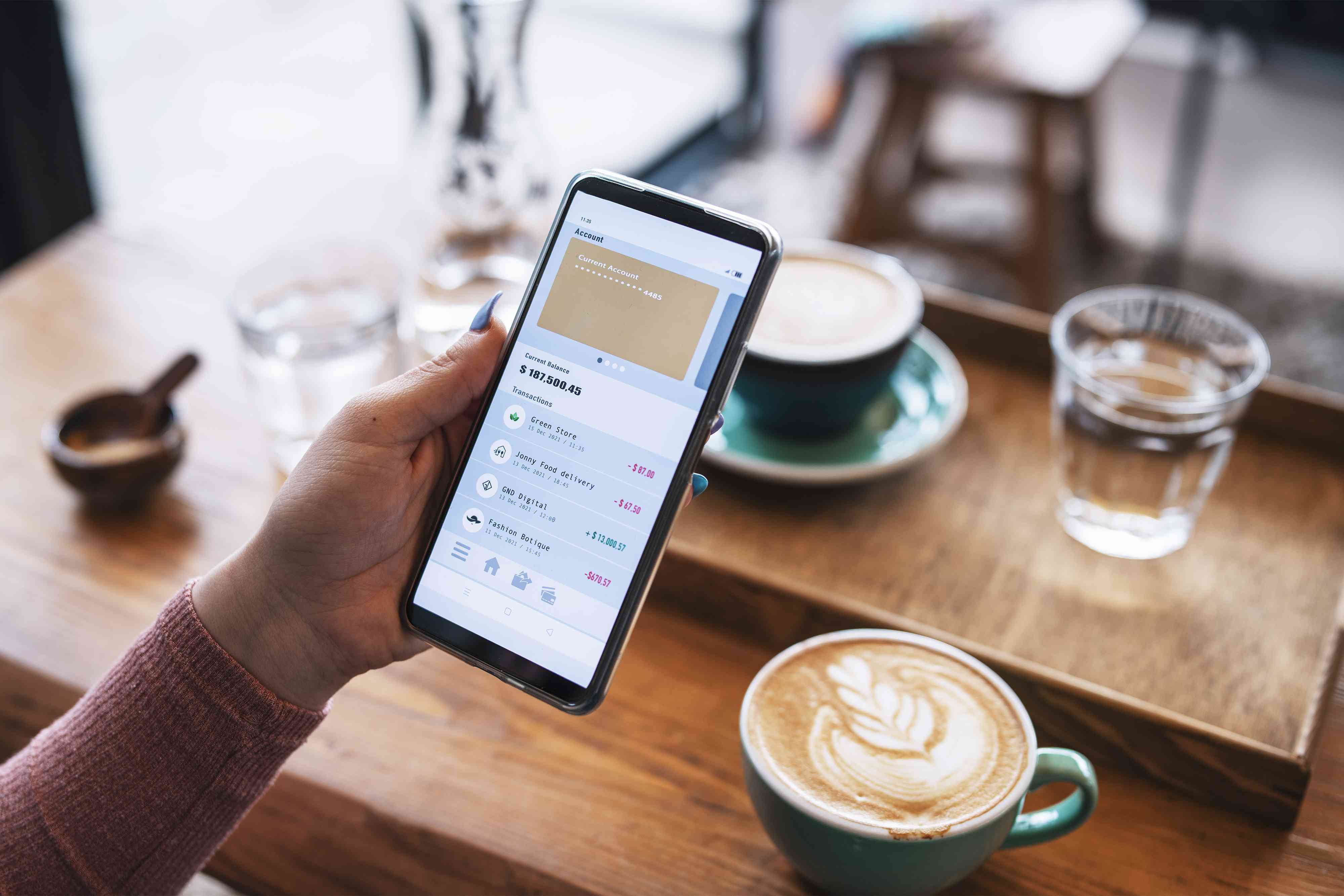 Shot of young woman managing bank account on smartphone at cafe