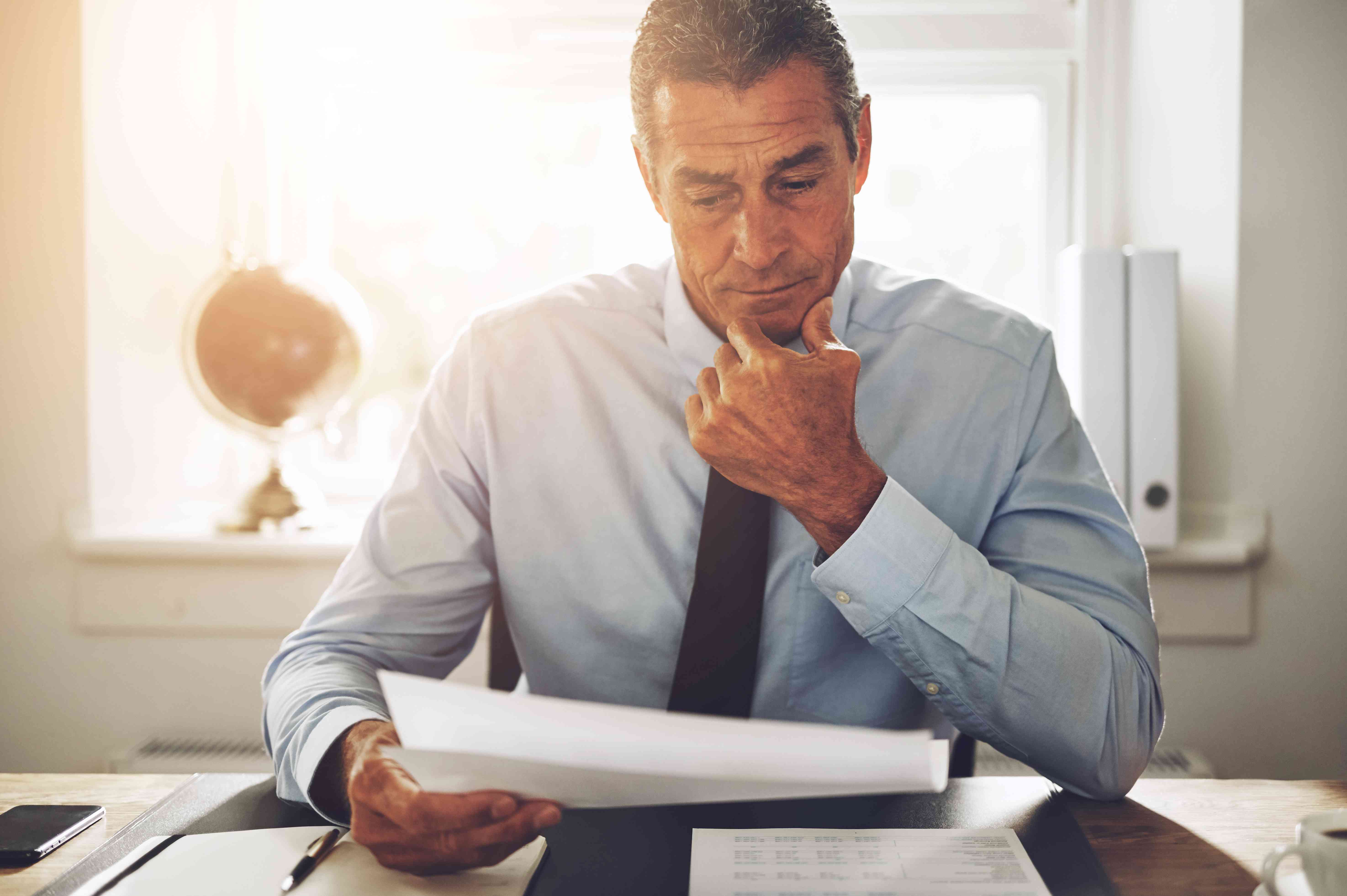 A mature investor rubs their chin as the look at an announcement from a bond issuer to call in a bond and pay yield maintenance premiums.